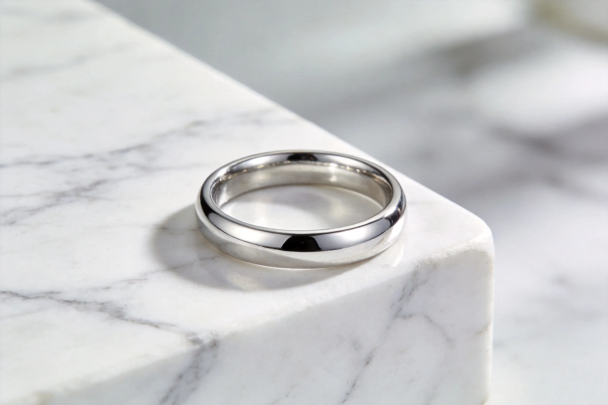 A sleek silver ring placed on a white marble surface, soft natural lighting, clean and minimalist composition, ultra-realistic, 8K, product photography style.