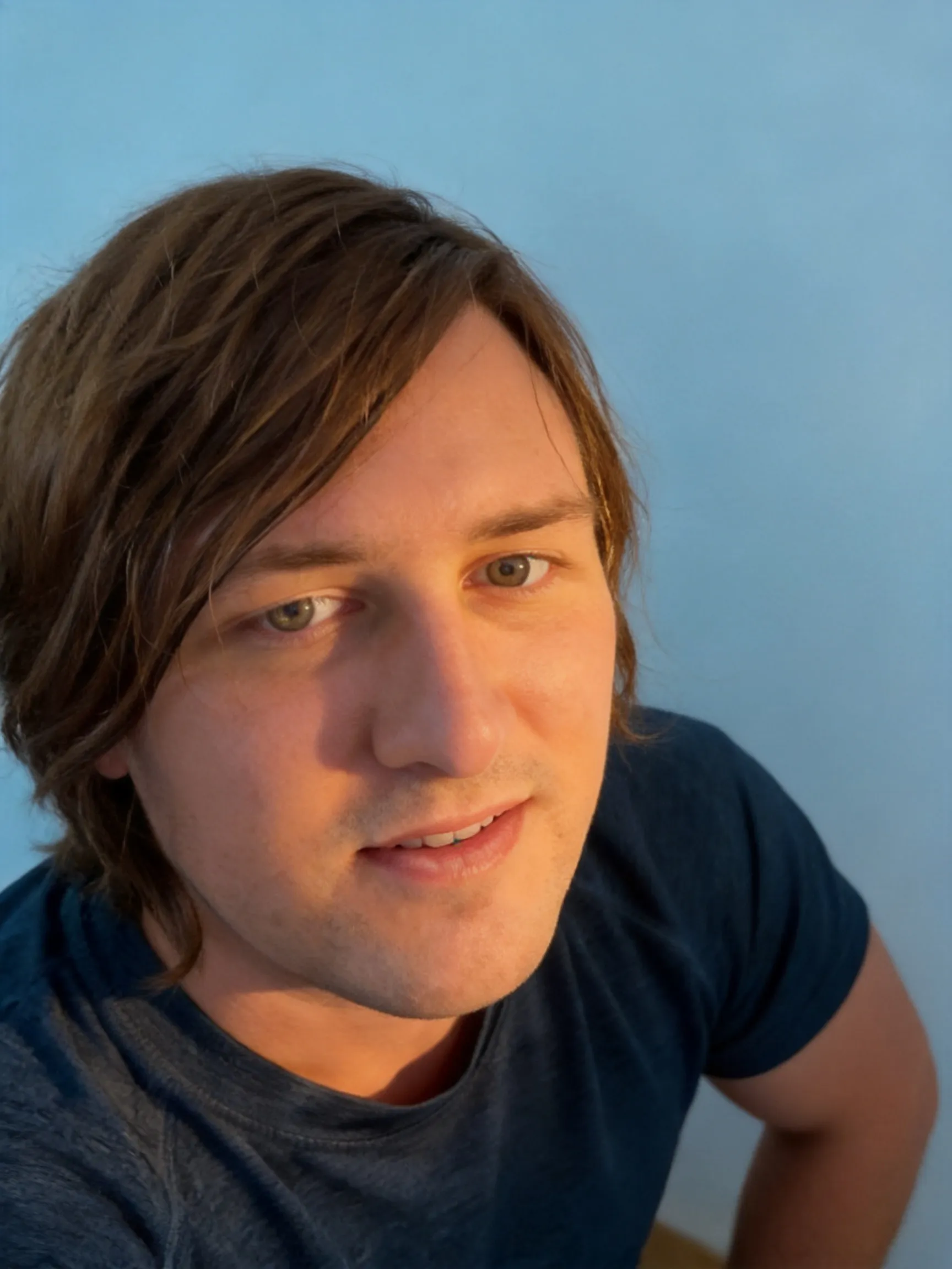 Make this the best profile picture ever. Make the lighting warm and cozy but not too extremely warm.  Make the lighting perfect. Make the angle epic and the face is in a very heroic pose. Make the wall behind him a soft baby blue. Make his eyes well lit so they are focal points on the image.