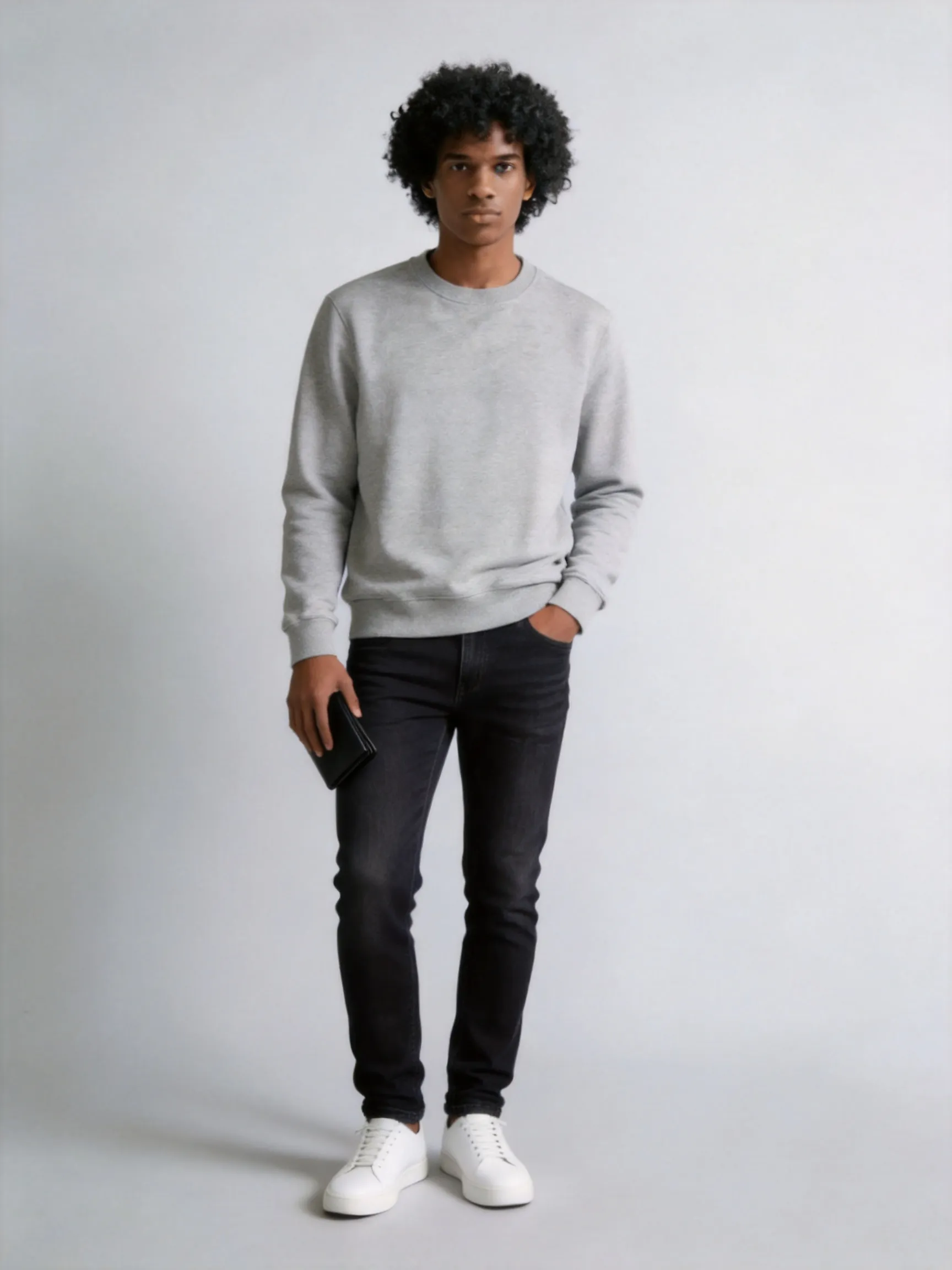 Full-body fashion photo of the identical female model, keeping same face, hair, body proportions, and pose. Men's style outfit worn as boyfriend-style: she wears a relaxed-fit heather grey crewneck sweatshirt and slim-fit dark wash jeans, paired with classic white leather sneakers, holding a black leather wallet. Clean casual aesthetic, realistic cotton sweater wrinkles, natural lighting on a light grey background.