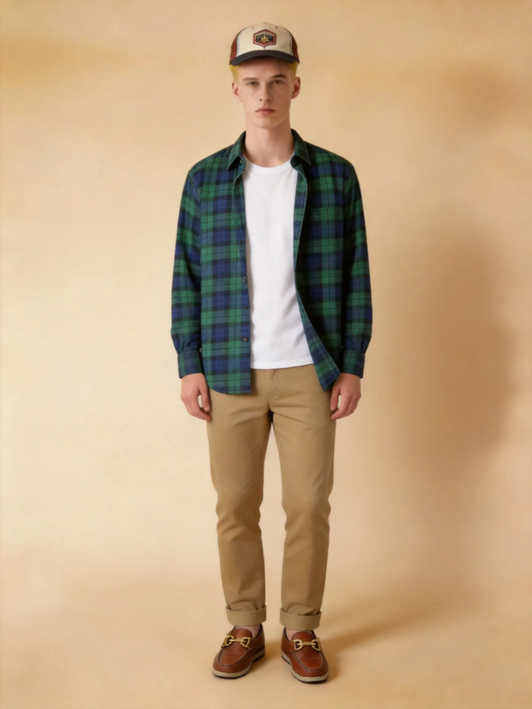 Full-body fashion photo of the identical female model, keeping same face, hair, body proportions, and pose. Men's style outfit worn as boyfriend-style: she wears an unbuttoned green and blue plaid flannel shirt over a white t-shirt, paired with khaki chino pants and brown leather boat shoes, wearing a retro baseball cap. Warm studio lighting, realistic flannel texture, American retro aesthetic, shot on a clean solid warm beige background.