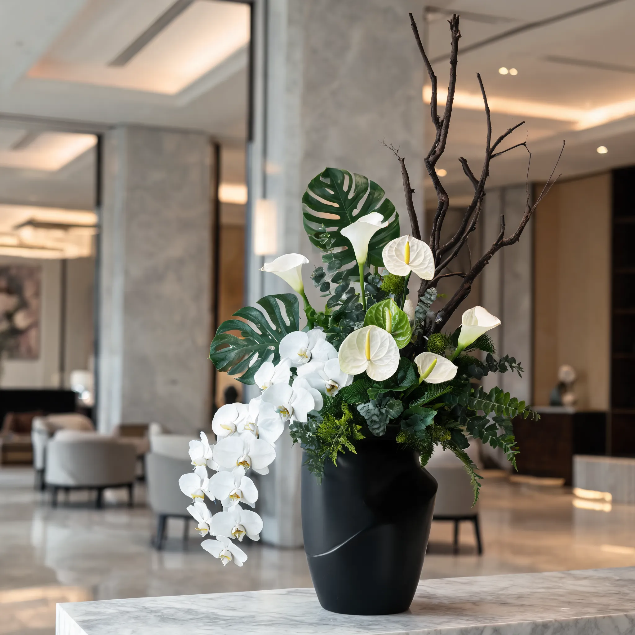 A modern luxury floral arrangement featuring white phalaenopsis orchids, anthuriums, calla lilies, monstera leaves, tropical foliage, sculptural branches, and premium greenery, arranged in a matte black designer vase, contemporary asymmetrical composition, high-end hotel lobby floral installation, clean architectural lines, sophisticated styling, realistic fresh flowers, editorial photography, ultra detailed, photorealistic, 8K