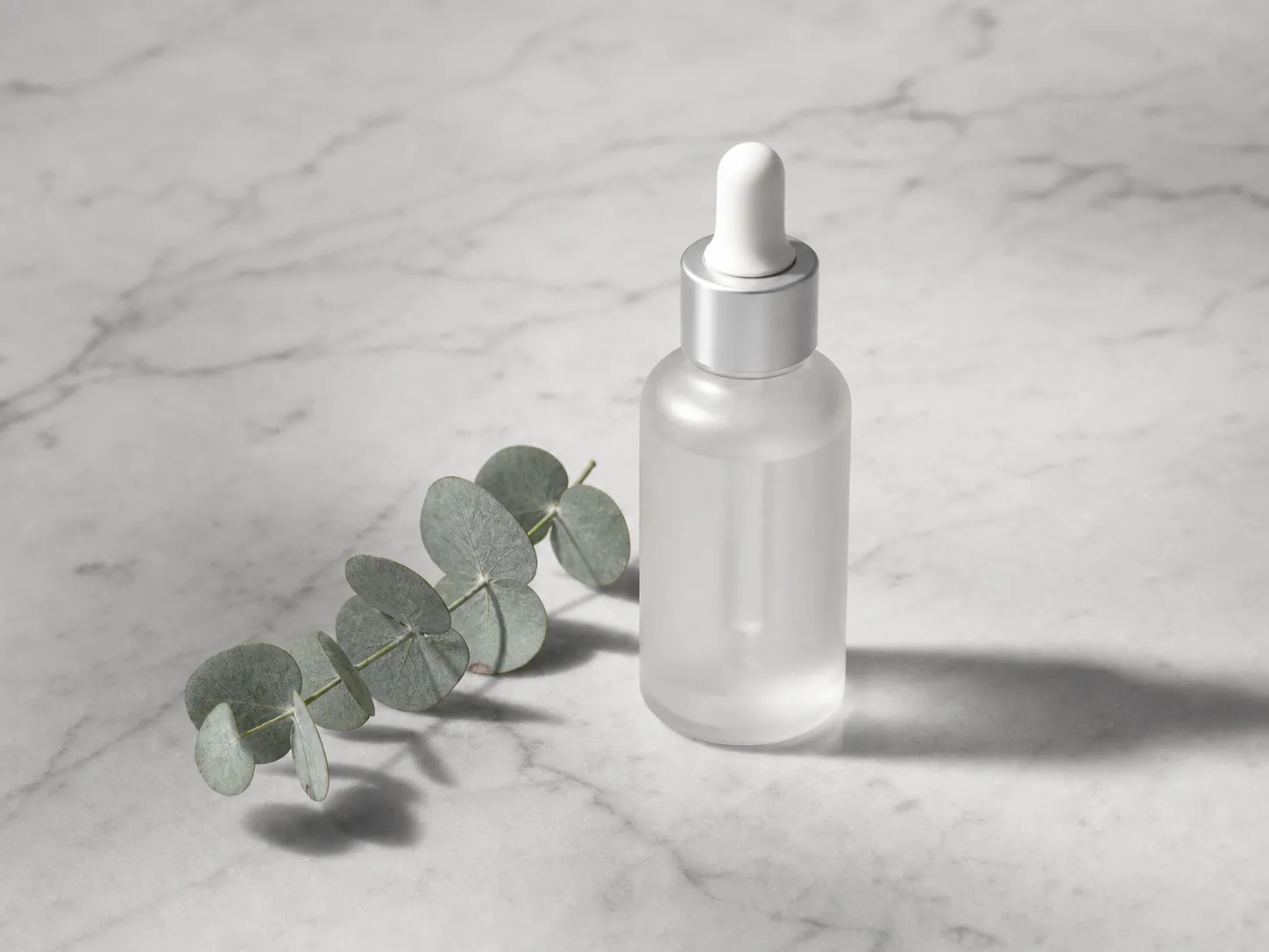 Minimalist product photography, a frosted glass skincare bottle placed on a light gray marble tabletop, next to a fresh eucalyptus leaf, soft top lighting, clean and sharp shadows, premium feel, low saturation, Morandi color scheme, clean background.