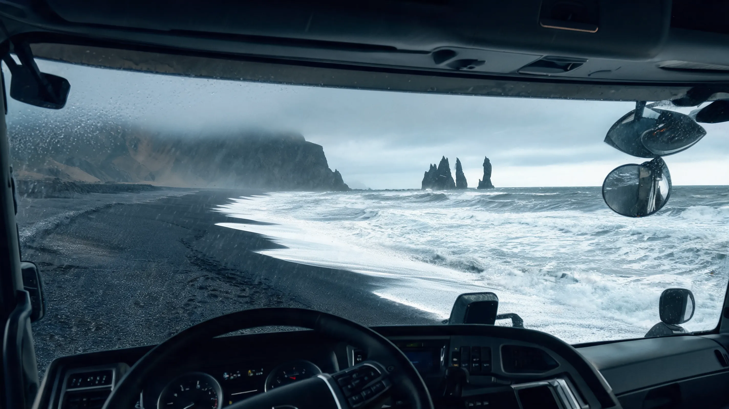 A photorealistic wide shot from the cab of a truck driving along Iceland`s black sand beach, Reynisfjara, with the dramatic basalt sea stacks Reynisdrangar rising from the churning Atlantic Ocean, moody grey sky, rain mist, volcanic cliffs in the background, ultra detailed, 8k.