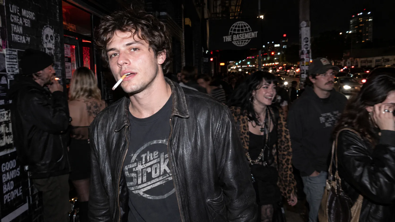 A spontaneous nighttime street photograph of a young American man leaving a crowded underground music venue. A direct on-camera flash sharply illuminates his face and clothing while the surrounding environment remains dark and slightly underexposed. Behind him, colorful city lights, passing cars, cigarette smoke, and blurred pedestrians create layered background activity. The flash produces realistic hard-edged shadows and subtle skin highlights rather than beauty lighting. Slight motion blur appears on people moving behind him. Raw documentary photography, high-ISO texture, authentic candid moment, imperfect framing.