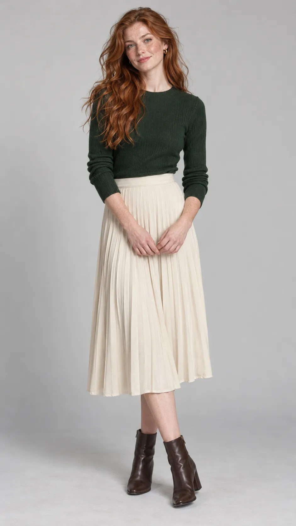 Create a photorealistic full-body studio portrait of a 27-year-old Irish woman, approximately 170 cm tall, with a naturally slender but healthy figure, very fair skin covered with delicate freckles across her nose and cheeks, pale green eyes, and long copper-red hair in loose, slightly untamed waves. She wears a forest-green fitted knit top, a high-waisted cream pleated midi skirt, small gold earrings, and dark-brown leather ankle boots with a modest heel. Her expression is warm and quietly confident, with minimal makeup that allows her natural complexion to remain visible. Her stance should feel like a real fashion model between poses, not a rigid mannequin. Soft neutral studio illumination, seamless light-gray background, gentle shadow beneath the boots, realistic freckles, flyaway hairs, knit fibers, and pleated fabric, high-end contemporary clothing catalog photography, accurate anatomy, full head-to-toe composition, vertical 9:16. No text, no watermark, no over-retouching.