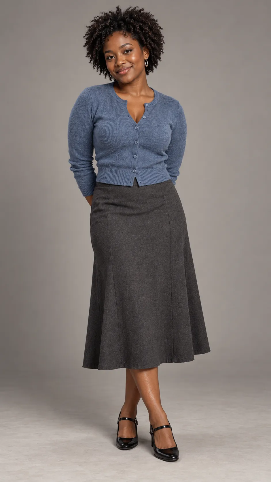 Create a photorealistic full-length studio portrait of a 26-year-old Black American woman, approximately 154 cm tall, with a petite, softly curvy build, rich dark-brown skin, warm brown eyes, and short, tightly coiled natural hair with a rounded silhouette. She wears a dusty-blue fitted knit cardigan, a high-waisted charcoal midi skirt, delicate silver earrings, and simple black Mary Jane heels. Her expression is cheerful but understated, with natural makeup and realistic skin texture. Maintain authentic petite proportions, natural limb lengths, and believable clothing fit. Soft commercial studio illumination, clean warm-gray background, gentle floor contact shadows, detailed knit fibers and individual curls, inclusive premium fashion catalog photography, full body visible from head to shoes, vertical 9:16 composition. No text, no watermark, no artificial skin lightening.