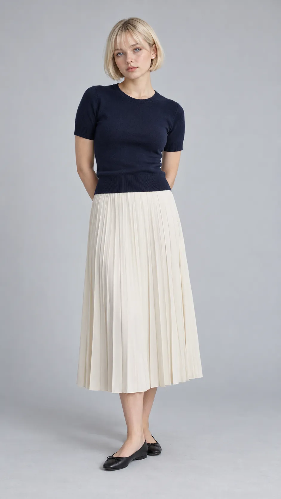 Create a photorealistic full-body commercial fashion photograph of a 24-year-old Swedish woman, approximately 156 cm tall, with a petite straight figure, fair cool-toned skin, blue-gray eyes, and a precise pale-blonde bowl bob with softly rounded edges. She wears a navy-blue fitted knit top, an ivory pleated midi skirt, small silver stud earrings, and black ballet flats. Her expression is neutral and modern, with natural skin texture and minimal makeup. Preserve her petite proportions and realistic head-to-body scale. Use a seamless cool light-gray background, soft diffused lighting, gentle contact shadows, accurate pleat structure, realistic hair strands, and clean Scandinavian e-commerce photography. Full body visible from head to shoes, vertical 9:16. No text, no watermark, no oversized head or artificially elongated legs.